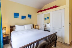 Cozy bedroom with a king-sized bed, complemented by vibrant beach-themed artwork. Features a mirrored closet, stylish lighting, and ample storage with a lofted space above, creating a comfortable and functional retreat.
