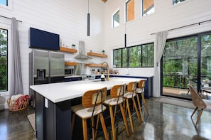 Chef’s kitchen features oversized island, modern appliances, and forest views.