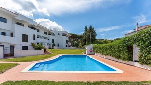 Sparkling pool surrounded by lush greenery and white buildings. Ideal spot for refreshing dips and sunbathing in a tranquil setting. #Poolside #OutdoorOasis #SunnyDays #VacationVibes #Relaxation