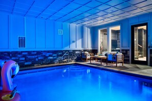 This stunning indoor pool area features vibrant blue lighting, a relaxing seating lounge, and large windows bringing in natural light.