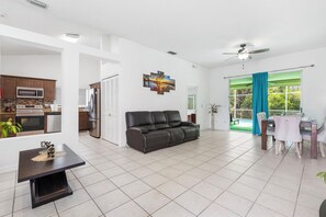 Bright and spacious open-concept living and dining area with tile flooring, direct access to the screened-in pool patio, and a view into the modern kitchen — ideal for relaxing and entertaining.