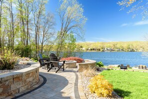 Lakeside stone patio with fire pit and chairs, perfect for relaxing views.