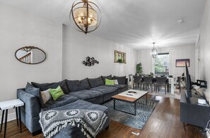 Comfortable living room with cozy sofas, a smart TV for entertainment, two single chairs for reading or conversation, and classic games like Connect 4, Jenga, and Scrabble.