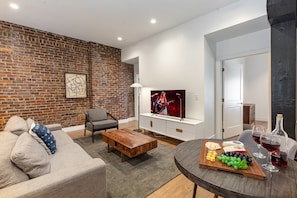 The living room features an open-concept design with a charming brick wall, cozy seating, and a Smart TV for relaxing nights in.