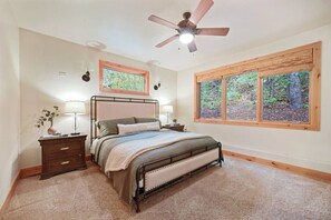 Master bedroom featuring a comfortable king-size bed, soft carpet, and large windows with beautiful forest views.