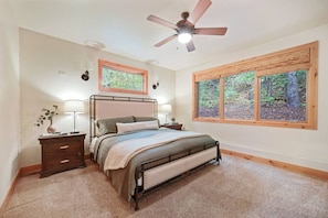 Master bedroom featuring a comfortable king-size bed, soft carpet, and large windows with beautiful forest views.