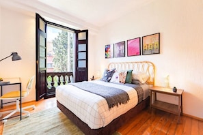 Bright bedroom featuring a queen bed with soft natural light streaming through large windows.
