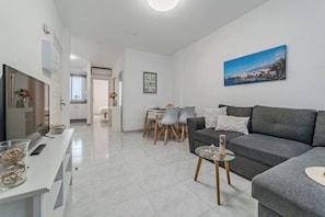 Open-Concept Living Area with a Dining Table, Sofa-Bed, AC and Smart TV.