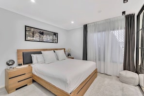 Step into the primary bedroom and sink into the king bed, with a soft rug underfoot, blackout curtains for restful sleep, and direct access to a private ensuite.