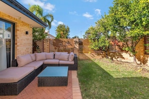 Soak up the sun in the lush front yard, where a cushioned outdoor couch invites relaxation beside citrus trees, perfect for morning coffee or evening wine.