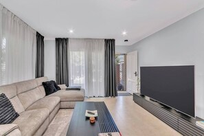 Step into a calming living area where an L-shaped sofa, blackout curtains, and a cinema-style smart TV create a perfect setting for cosy streaming nights.