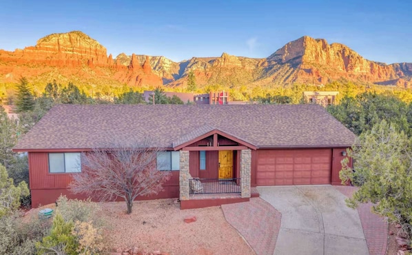 A charming home nestled among desert landscape with striking red rock formations in the background, bathed in warm sunset light.