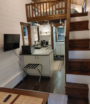 Tiny home kitchen and stairs to loft queen bedroom.Kitchen has microwave, fridge with freezer, Toaster oven and induction cooktop.TV turns towards sitting area.