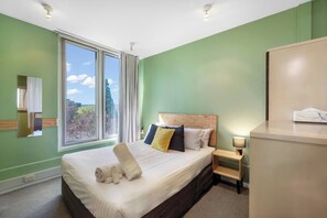 Rest easy in a simply furnished bedroom with a queen-size bed, soft linens, and large windows framing peaceful views of St David’s Park.