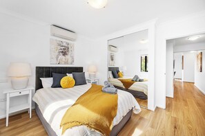 
Bright and inviting bedroom featuring a comfortable bed with a yellow throw and stylish accents. Includes an air conditioner, bedside tables with lamps, and mirrored built-in wardrobes for convenience.
