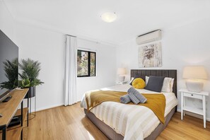 Bright, comfortable bedroom with a plush bed, air conditioning, and a TV. Features modern white and wood decor for a relaxing stay.