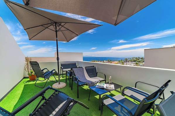 Relax on a Sunny Rooftop Terrace with Panoramic Ocean Views, Comfy Loungers, and Shades — your Perfect Holiday Spot.