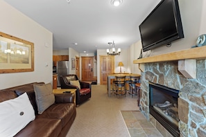 The living area features a queen sized sleeper sofa, mounted TV over a stone fireplace, and access to the patio.