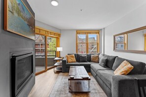 The living area features a mounted smartTV over a gas fireplace, a queen sleeper sofa, and access to the balcony.