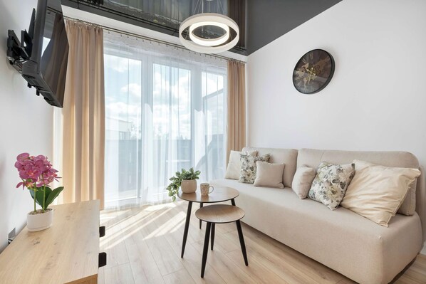 A cozy living room featuring a beige sofa, coffee table, and decorative plants near a large window.