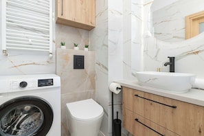 A bathroom with a washing machine, sink, and wooden cabinetry with white tiled walls.
