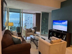 Bright and cozy living room with ocean views, comfortable seating, and a large TV for your entertainment. Relax with natural light and enjoy the fresh breeze from the balcony—your ideal spot to unwind.