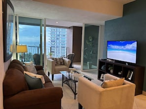 Bright and cozy living room with ocean views, comfortable seating, and a large TV for your entertainment. Relax with natural light and enjoy the fresh breeze from the balcony—your ideal spot to unwind.