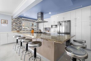 Fully equipped indoor kitchen with stainless steel appliances, island seating for 6, and dining space for 8—ideal for family meals and entertaining.