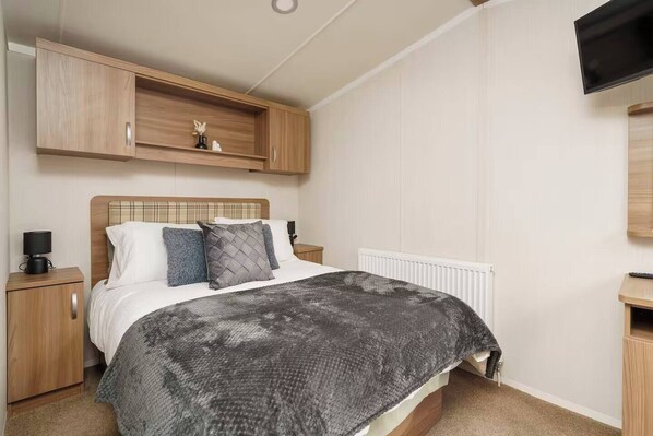 Comfortable double bedroom with plush bedding, ample storage, and a mounted TV. The space features modern wood accents and a calm, neutral palette for a restful night’s sleep
