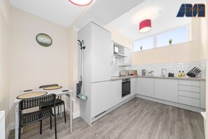Bright and modern kitchen-diner featuring sleek cabinetry, clean white tiles, and stylish wood-effect flooring. The compact dining nook adds a cozy touch, while large windows flood the space with natural light—making it perfect for both cooking and casual