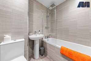 A modern bathroom with a sleek design, featuring a bathtub with a rainfall shower, elegant tiling, and fresh towels for a comfortable stay.
