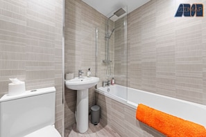A modern bathroom with a sleek design, featuring a bathtub with a rainfall shower, elegant tiling, and fresh towels for a comfortable stay.