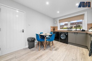 A stylish and modern kitchen with a sleek design, featuring neutral-toned cabinets, warm wood accents, and a dining area with vibrant blue chairs. A perfect space for cooking and enjoying meals together.