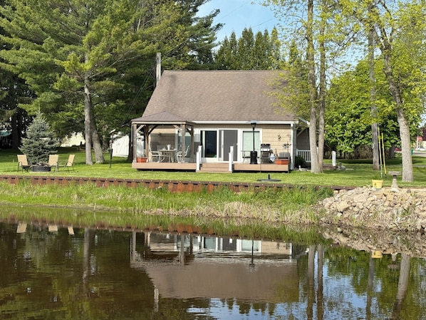 View of cottage from across the river. Riverside firepit on left.