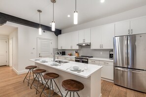 Kitchen with stainless steel appliances, white cabinetry and countertops, a central island, and breakfast bar seating for 4.