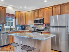 Granite island and wood cabinetry with stainless steel appliances and decorative backsplash.