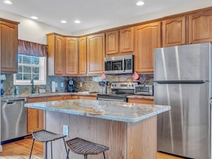 Granite island and wood cabinetry with stainless steel appliances and decorative backsplash.
