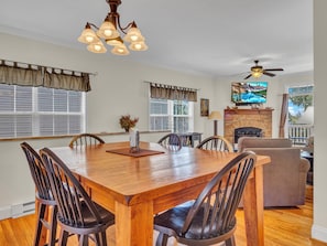 Open-concept layout with farmhouse dining table, cozy seating, stone fireplace, and TV.