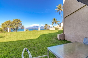 NAP-B43 Enjoy a peaceful morning coffee on the lawn with views of lush greenery and the nearby ocean peeking through the trees under a clear blue sky.