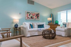 Coastal-inspired living room with vaulted ceiling, comfy white seating, smart TV, and tropical accents.