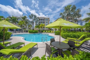 Resort-style pool surrounded by lush palms, vibrant lounge chairs, and shaded seating featuring a clubhouse.