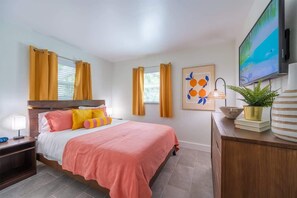 Bedroom with a queen bed featuring a wall-mounted TV, spacious dresser, double closet, and warm natural light through dual windows.