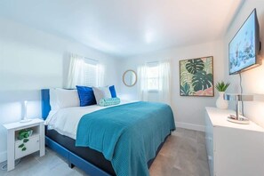 This bedroom features a queen bed with vibrant accent pillows, a flat-screen TV, nightstands, and a spacious closet. There's also an ensuite bathroom just steps away for added convenience.