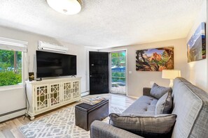 Step into comfort with a cozy living room featuring a Smart TV, plush seating, and views of the peaceful front yard.

