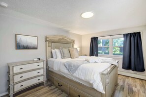 The bedroom offers a queen bed with fresh linens and calming decor, plus large windows that bring in natural light and peaceful views of the front yard.
