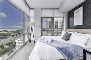 City views! Modern bedroom 1 featuring a king-size bed and large windows that let in plenty of natural light.