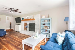 View from walking in from Front Door. Blue single-person futon, Electric Fireplace, Sectional, Roku TV, Games & Books in TV Console, plus Retro Arcade Game.