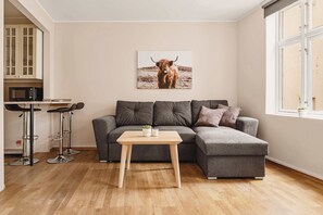 Modern living area with a cozy grey sectional sofa, warm wooden floors, and a touch of character with wall art and natural light.