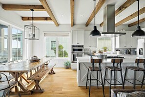 The kitchen is a culinary dream, boasting marble quartzite counters, a six-burner gas stove, island seating, and a rustic wood dining table, ideal for gathering with friends and family.