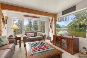 Enjoy lively board or card games in the inviting living room, where expansive windows frame the mountain views and a crackling fireplace sets the perfect cozy ambiance.